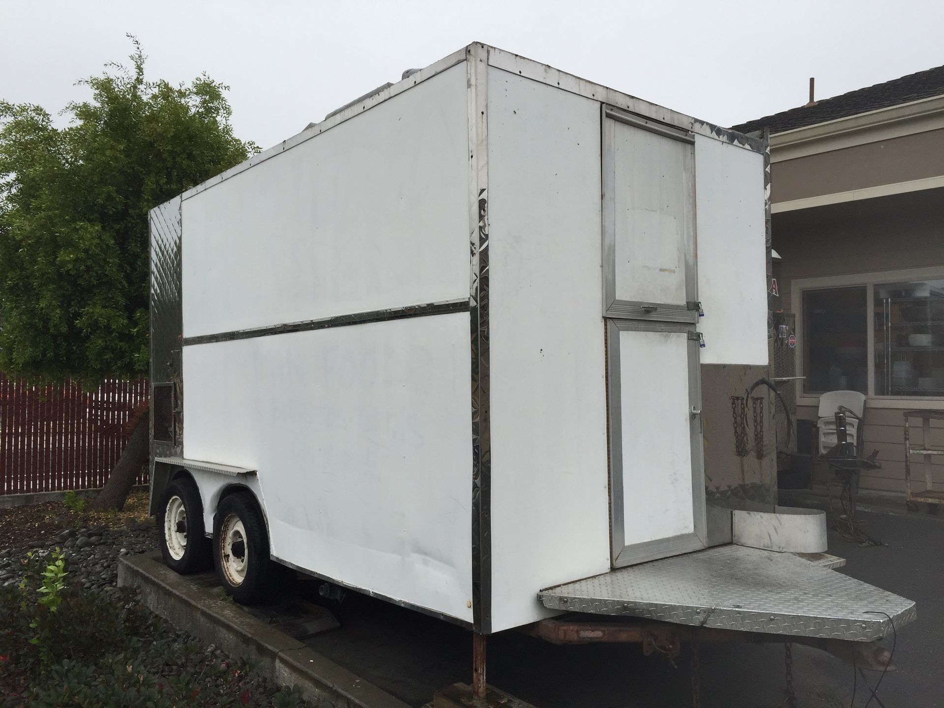 White enclosed trailer with side door and ramp parked beside a house.