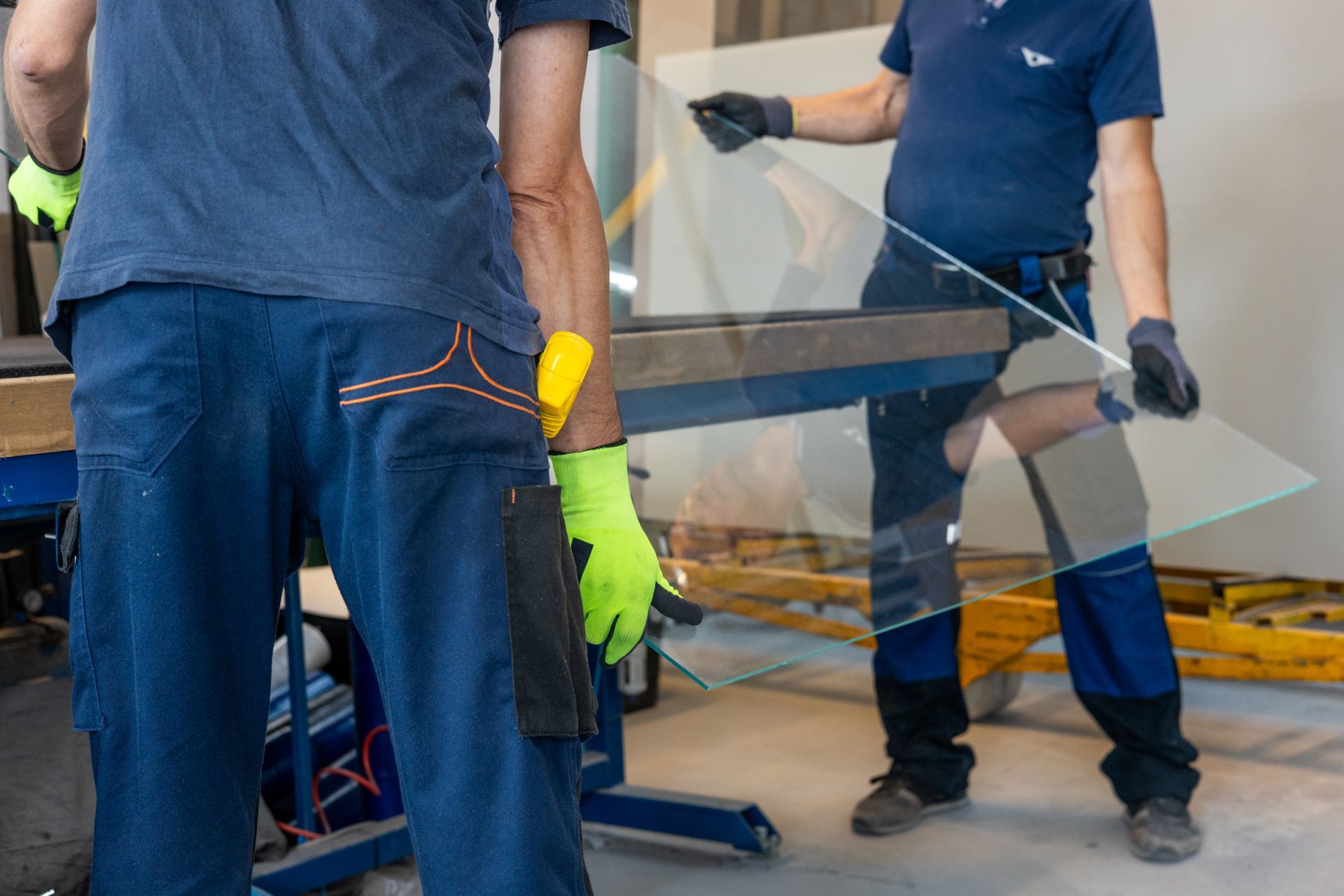 Workers in gloves handling a large glass panel in a workshop setting.