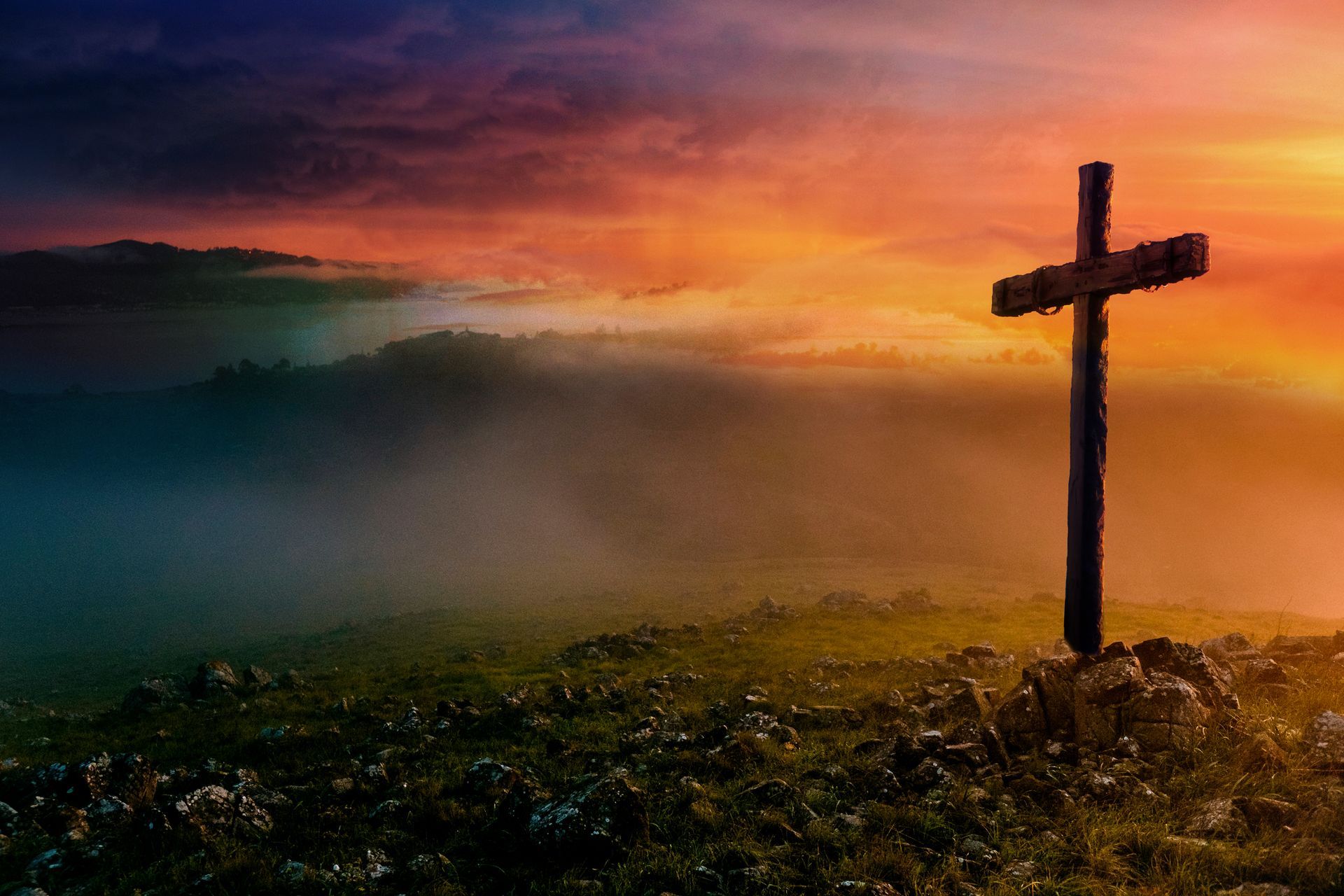 Silhouetted cross on a misty hill at sunset with orange sky and dark foreground