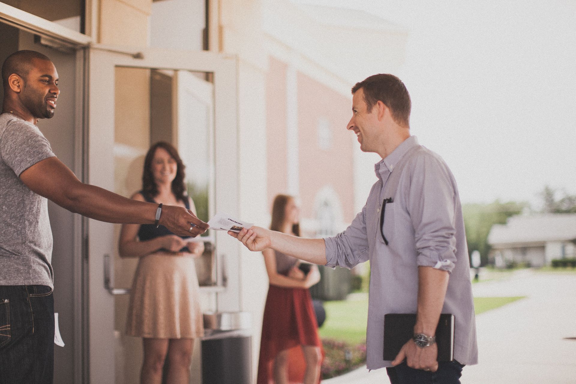 Two people exchanging keys outside a building, with two others waiting nearby.