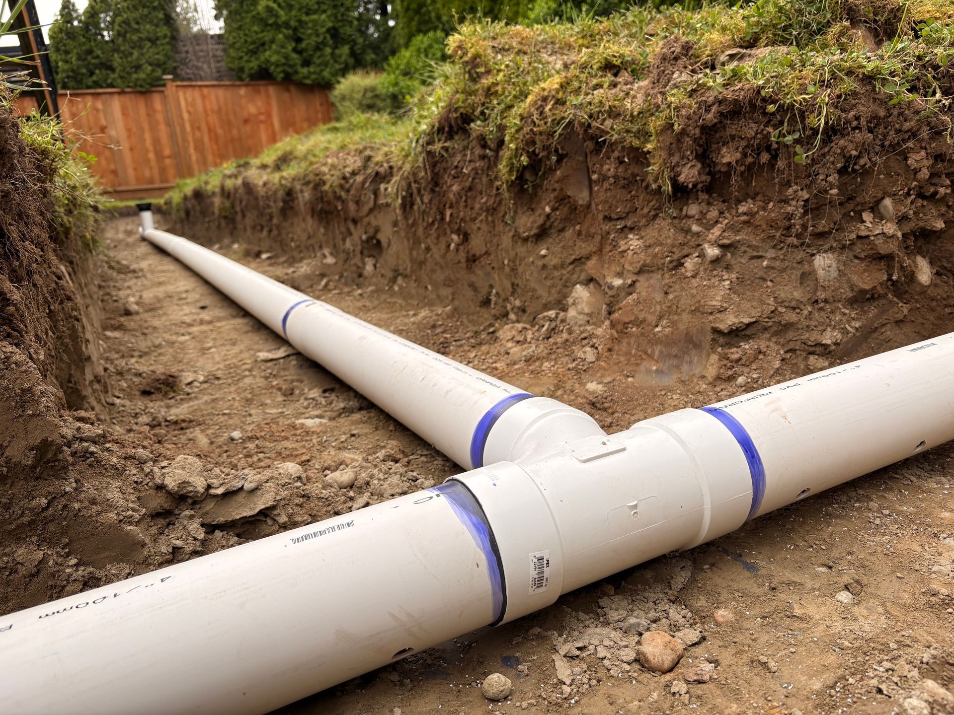 Large white PVC pipes laid in a dirt trench at a backyard