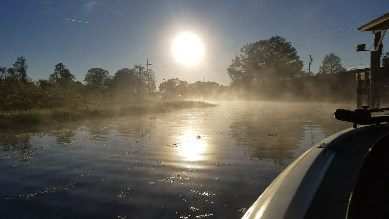 A boat is floating on a river with the sun shining through the fog