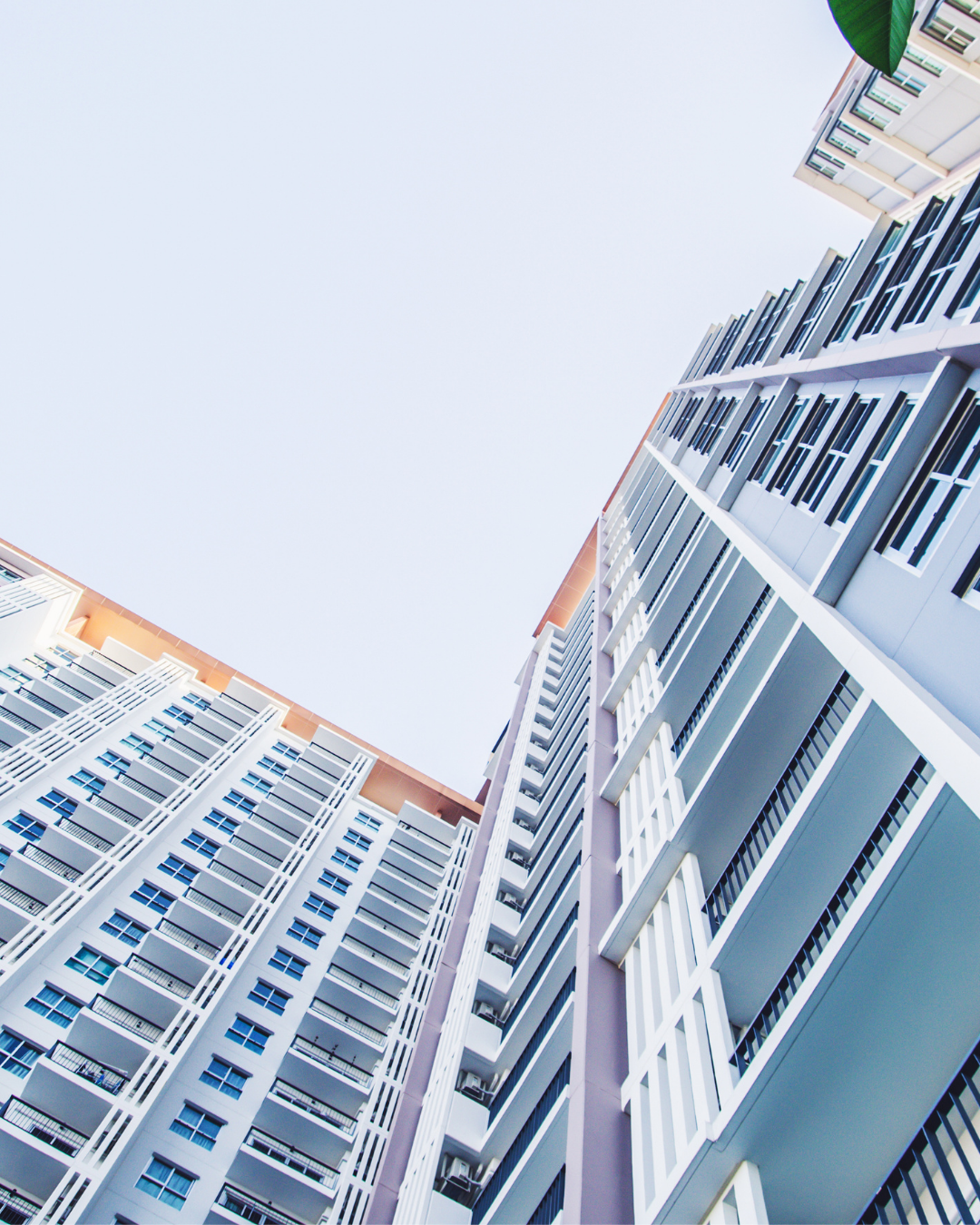 Olhando para cima, para os altos prédios de apartamentos brancos e azuis contra um céu pálido.