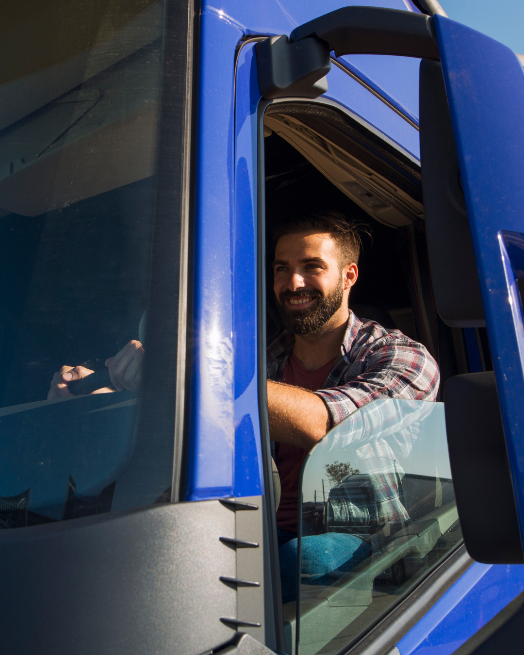 Homem barbudo sorridente na cabine de um caminhão azul, olhando pela janela aberta.