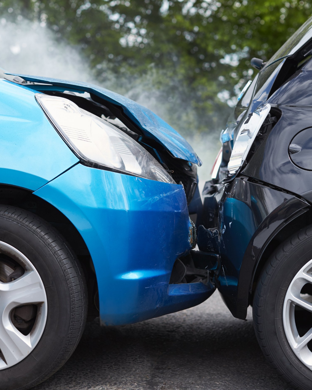 Dois carros, um azul e um preto, colidem frontalmente em uma estrada, com os para-choques danificados.