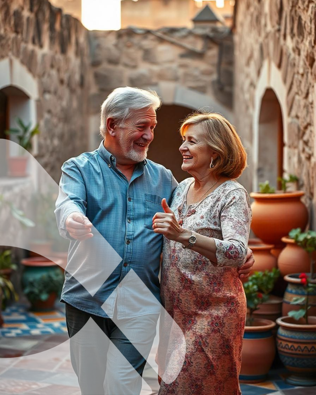 Casal sorridente dançando em um pátio ensolarado com vasos de plantas e arcos de pedra.