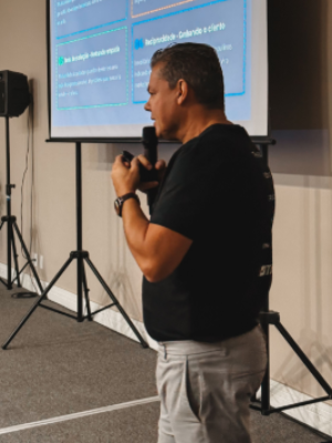 Man speaking into a microphone beside a projected presentation in a conference room