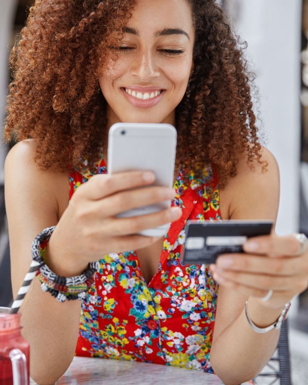 Pessoa sorridente usando um smartphone enquanto segura um cartão de crédito em uma mesa.