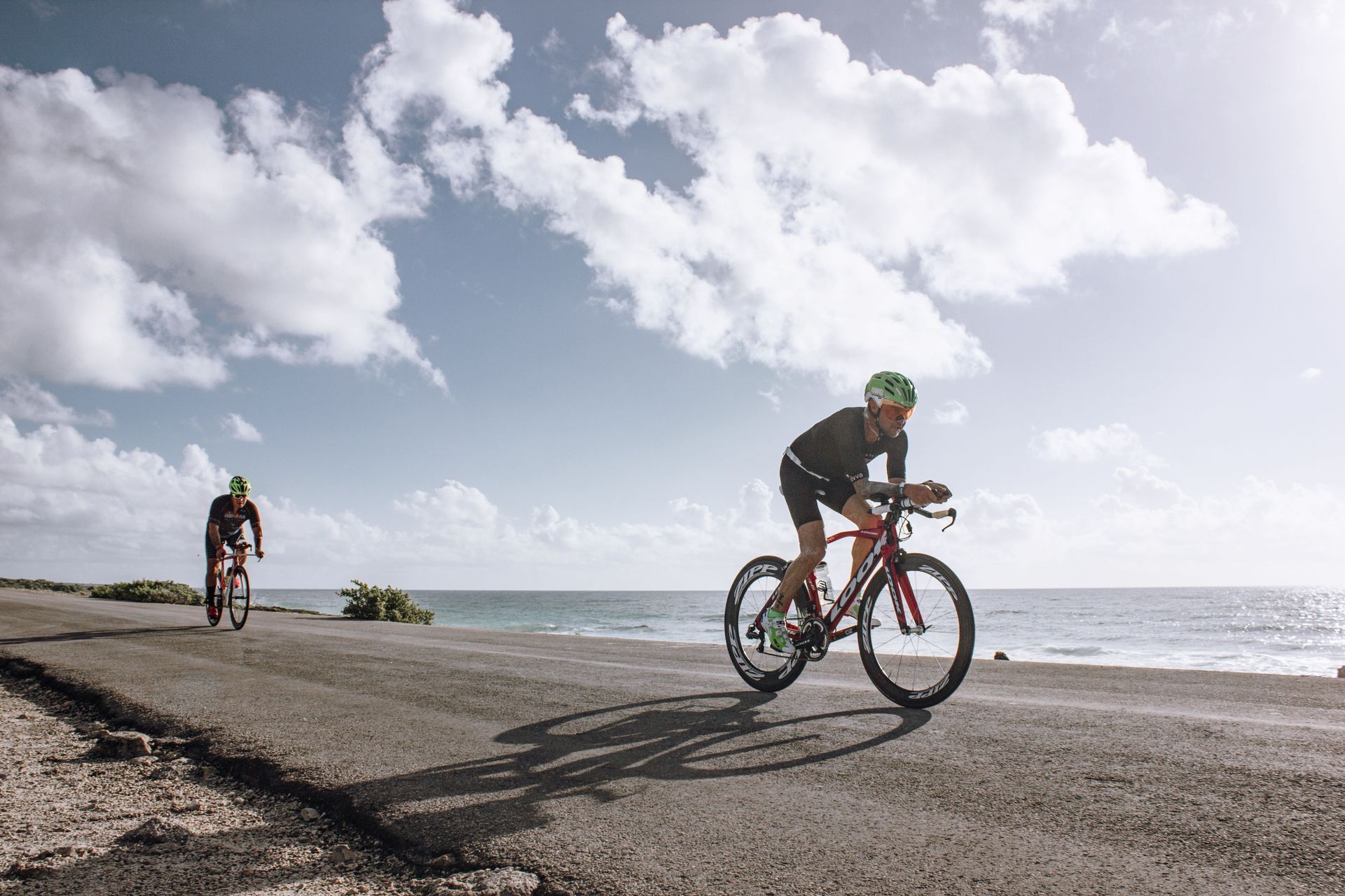 Ciclistas pedalando em uma estrada costeira à beira-mar sob um céu nublado.