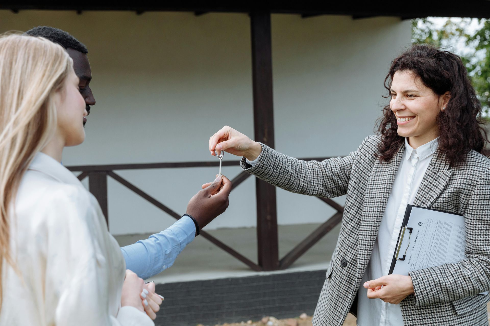 Two people exchanging keys outside a building, one smiling and holding a folder.