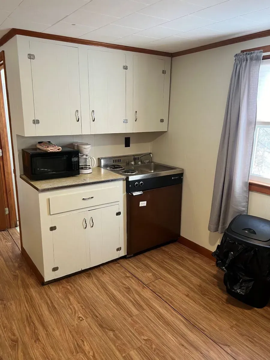 A kitchen with wooden floors , white cabinets , a microwave and a dishwasher.