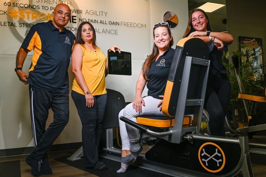 Four people posing beside an exercise machine in a gym, with one seated and smiling