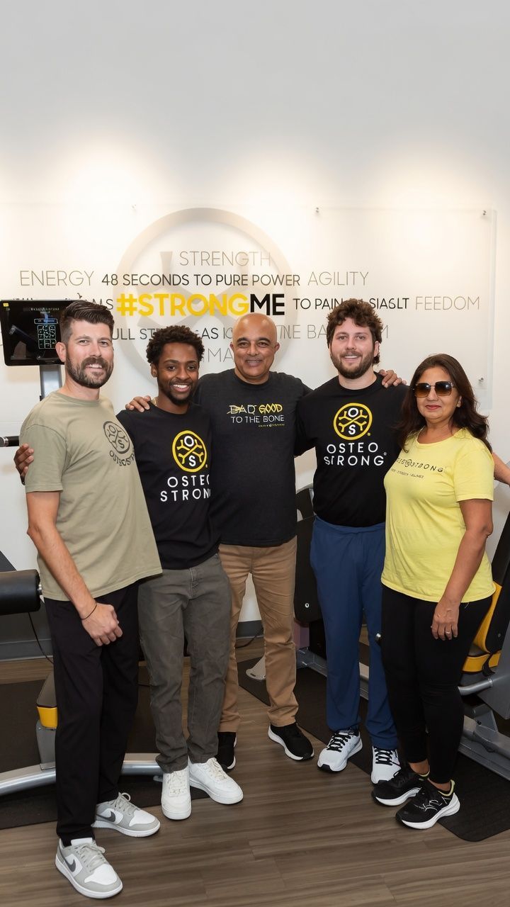 Five people pose indoors in front of a wall with gold text, smiling at the camera.