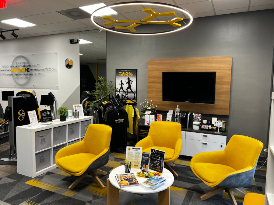 Modern office lounge with yellow chairs, round table, TV, shelves, and branded decor