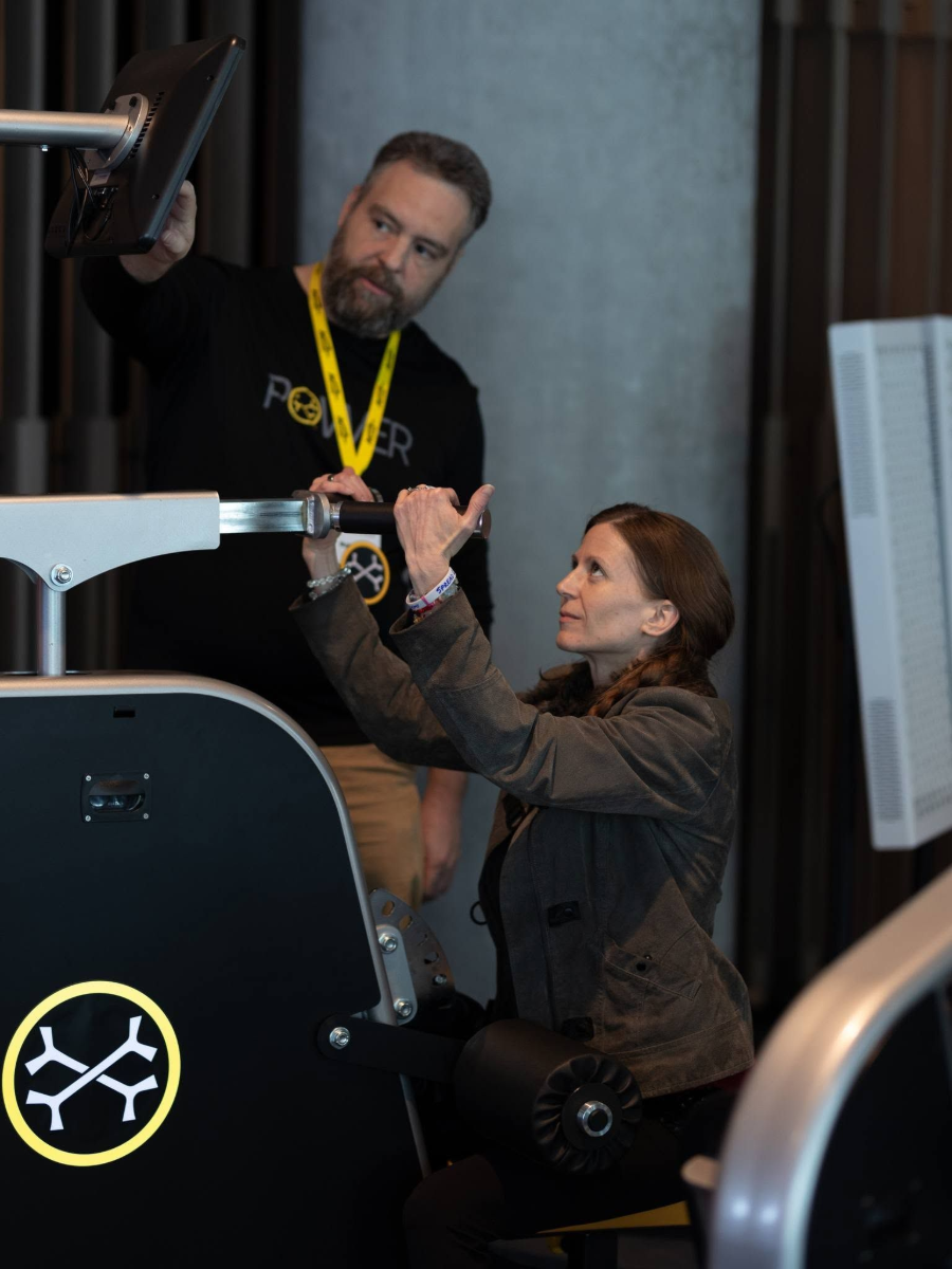 Two people adjusting a black machine with a yellow logo in a workshop-like setting
