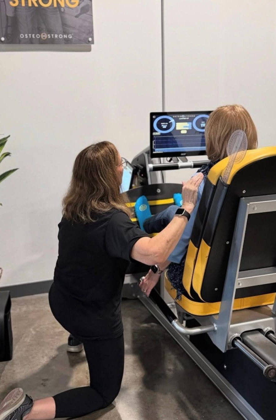 Person kneeling beside a seated rider, helping adjust controls on a virtual reality simulator console