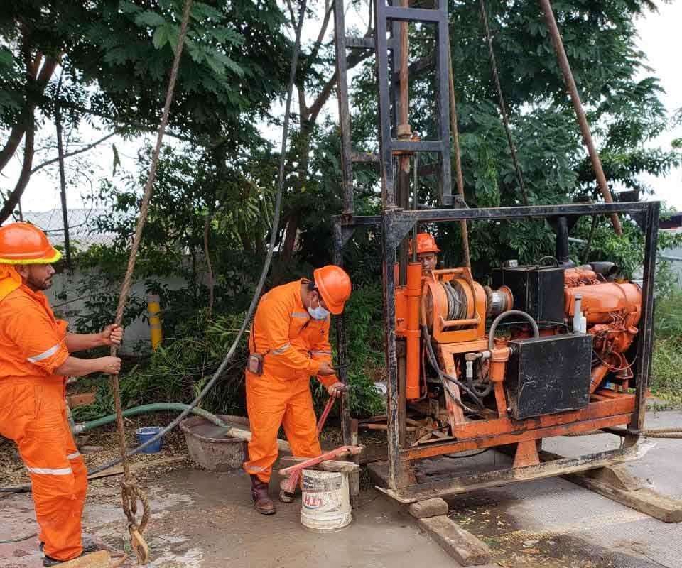 Los trabajadores con monos de color naranja operan una plataforma de perforación cerca de la vegetación.