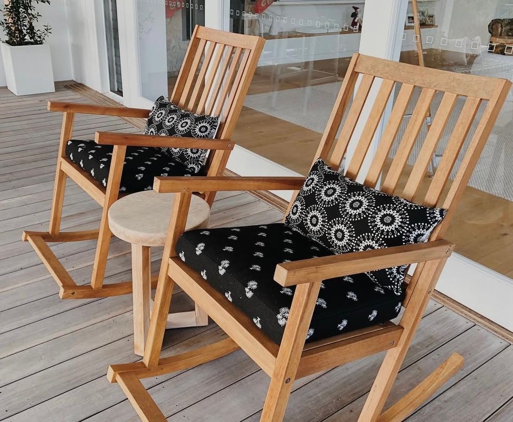 Two wooden rocking chairs with black patterned cushions and a small round table on a wooden deck.
