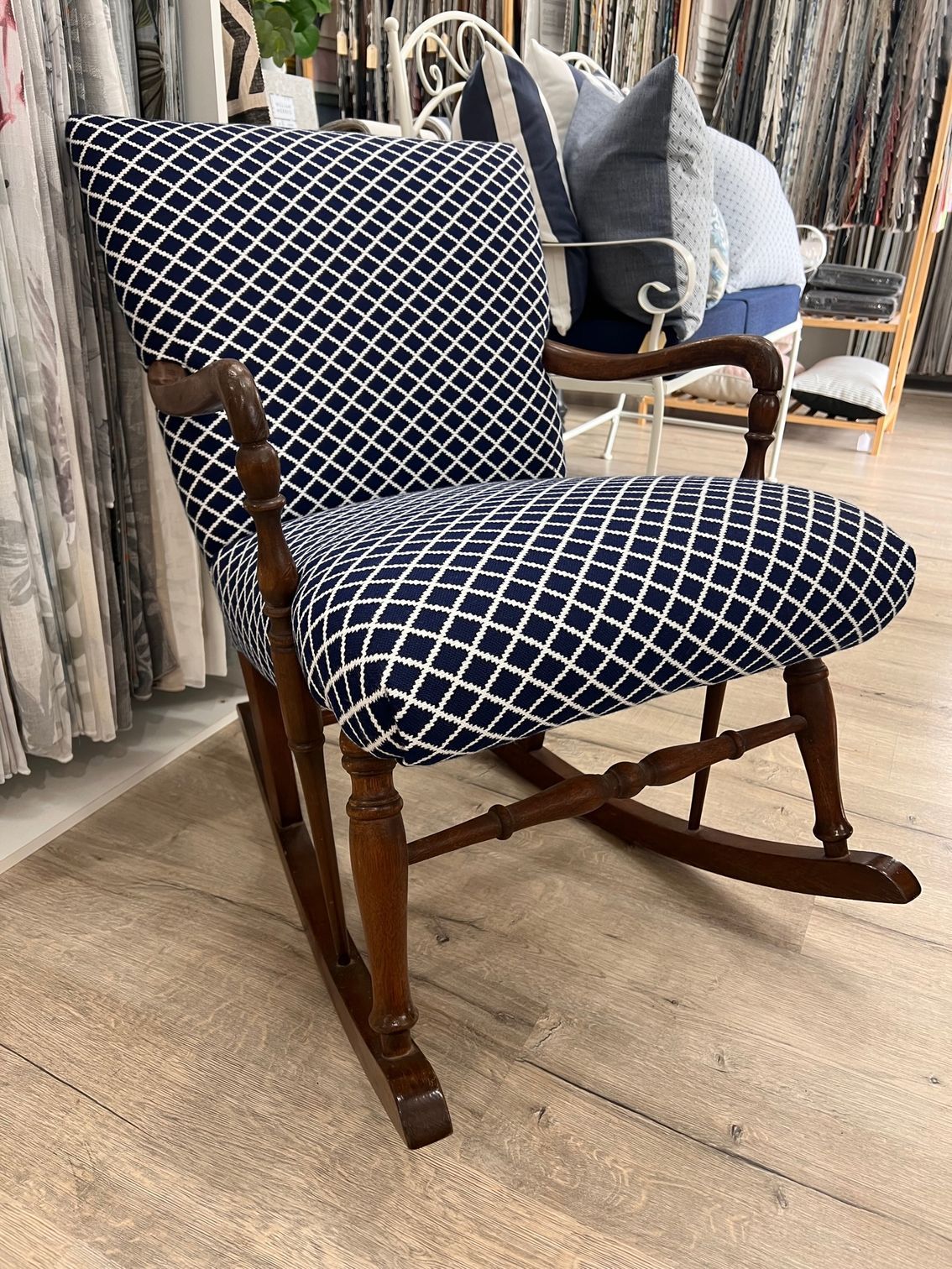 A wooden rocking chair upholstered in navy blue fabric with a white diamond grid pattern, situated in a store showroom.