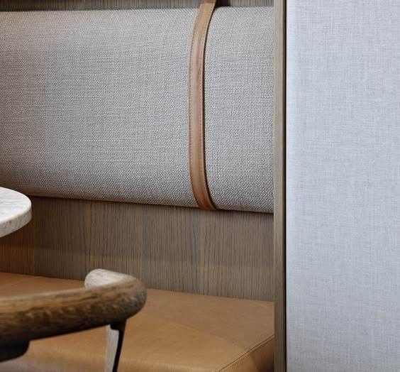 A close-up of a booth seat with a light gray fabric backrest, a brown leather seat, and a vertical leather strap accent.