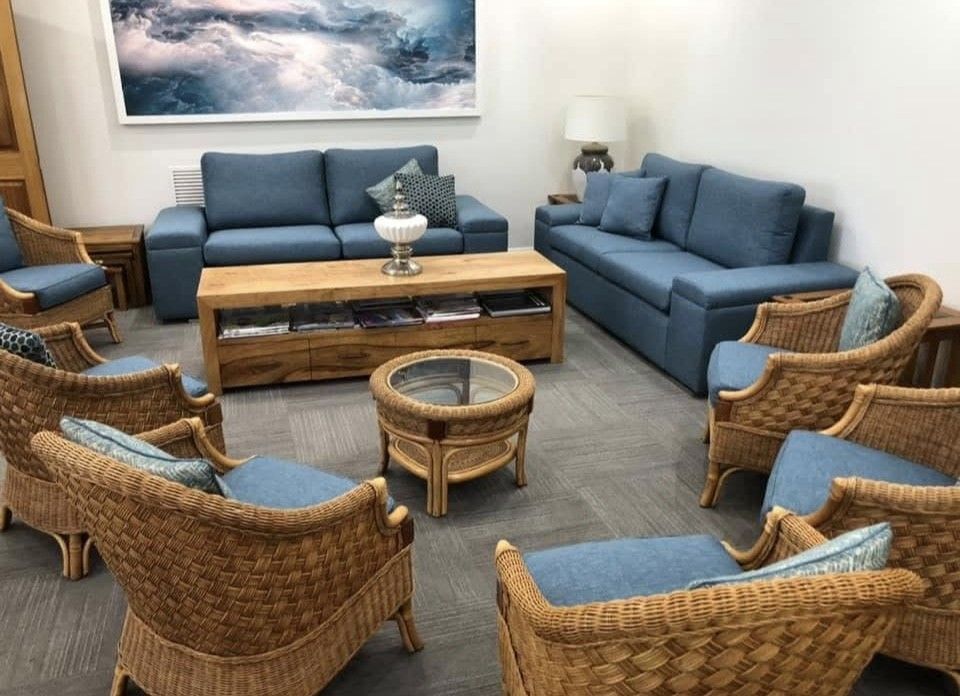 A living room setting featuring two blue sofas, a wooden coffee table, and several wicker armchairs with blue cushions.