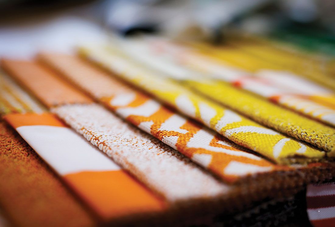 A close-up of folded fabric swatches in shades of orange, white, and yellow with various textures and patterns.
