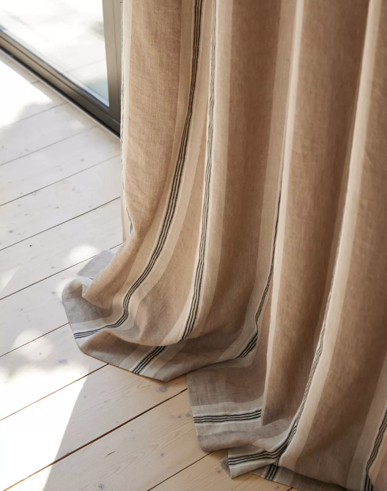 Floor-length linen curtains with vertical beige and white stripes hanging in front of a window and light wood floor.