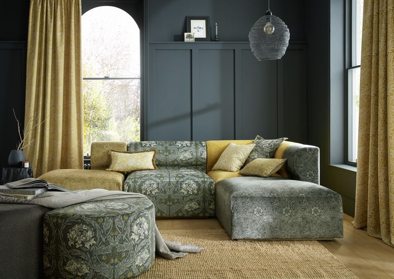 A living room with a modular patterned sofa and ottoman, mustard yellow curtains, and dark gray paneled walls.