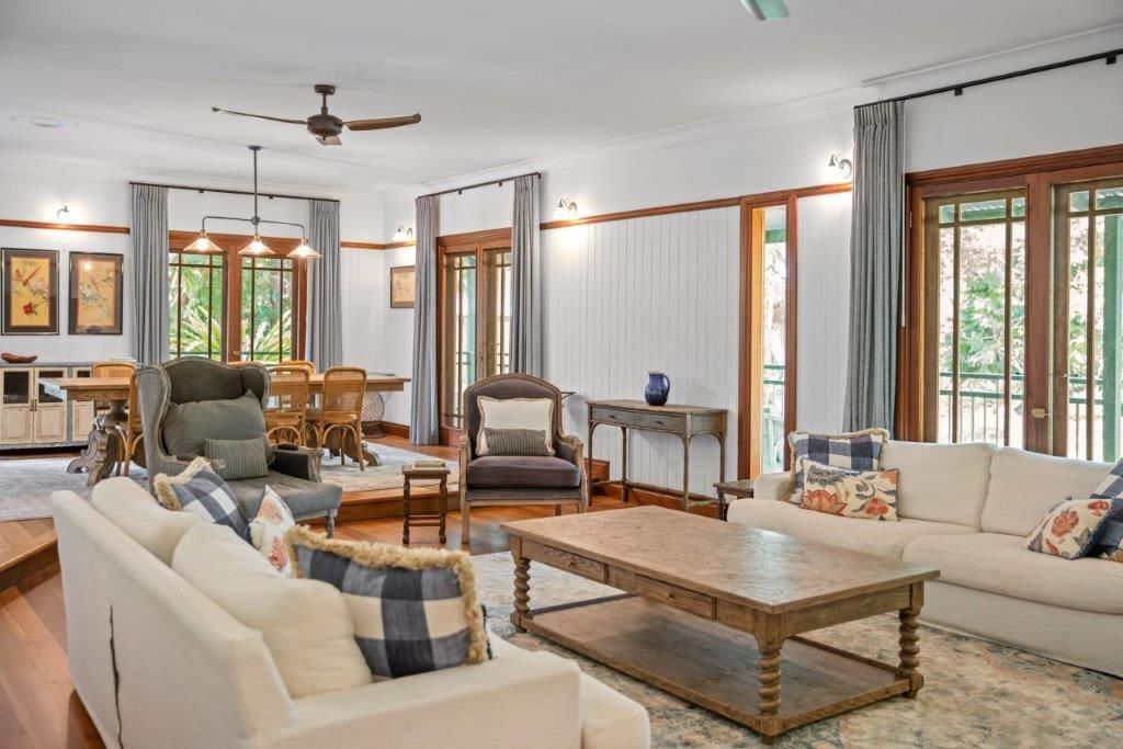 A spacious living and dining area featuring neutral furniture, a wooden coffee table, and large windows with grey curtains.