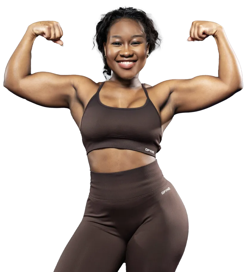 A woman in a green crop top and black shorts is smiling. Become Your Fit - Nikki