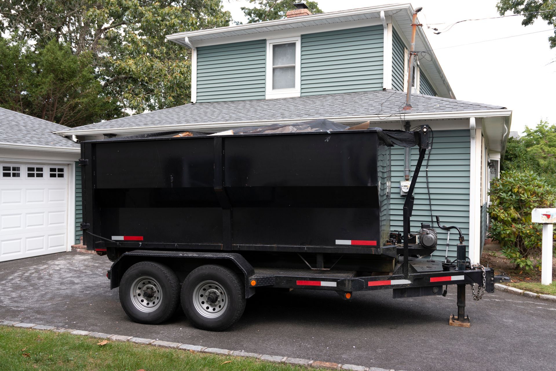 Trailer repair contractor inspecting black dump trailer parked in residential driveway.