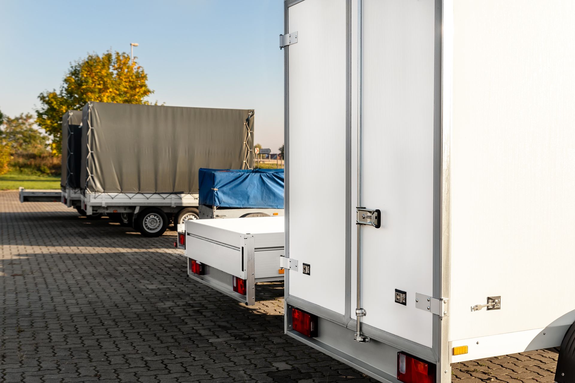 Many different types of small passenger car cargo freight trailers are parked in a row.
