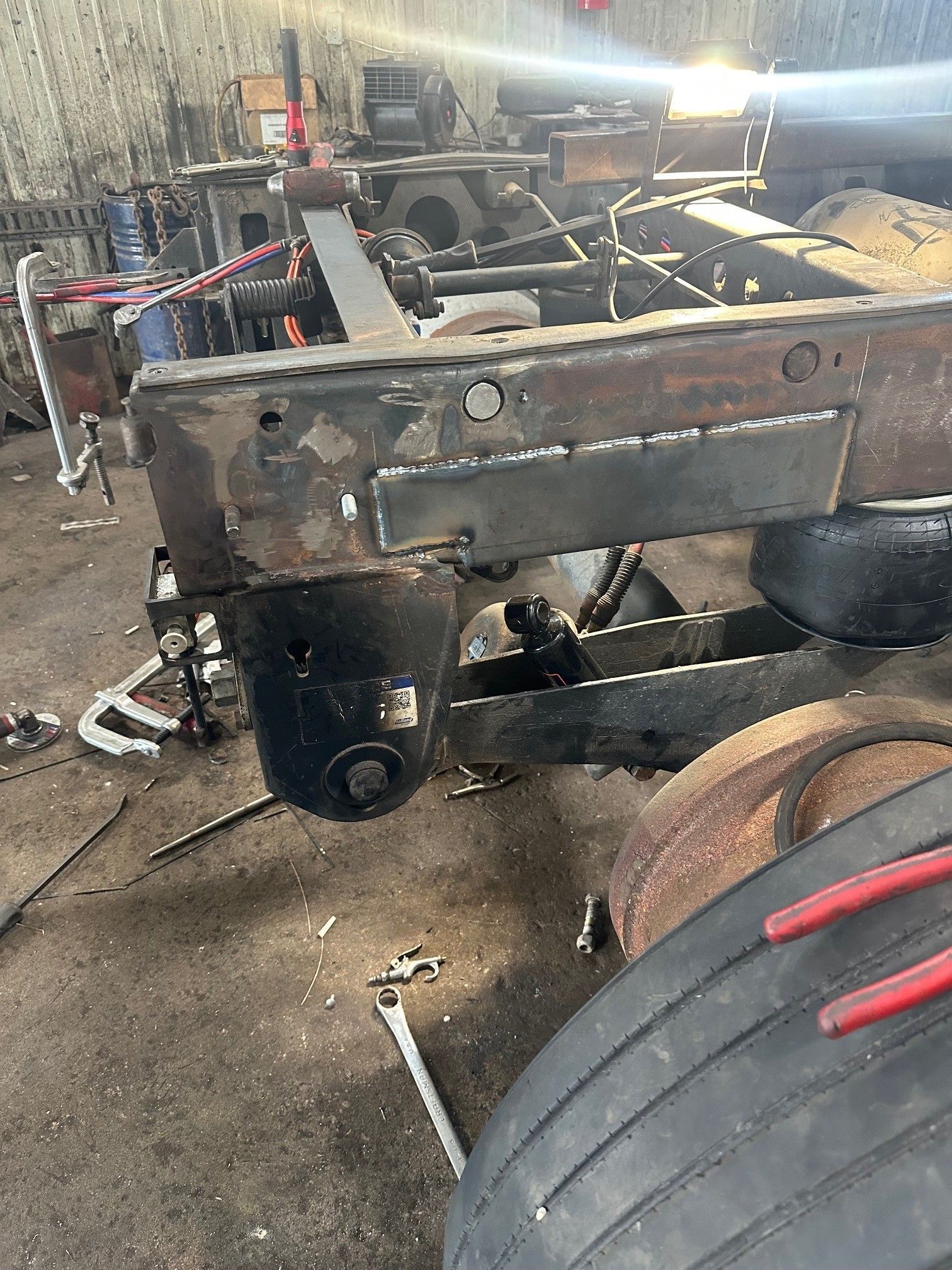 A close-up of a truck chassis undergoing frame repair, featuring a newly welded steel plate in a workshop setting.