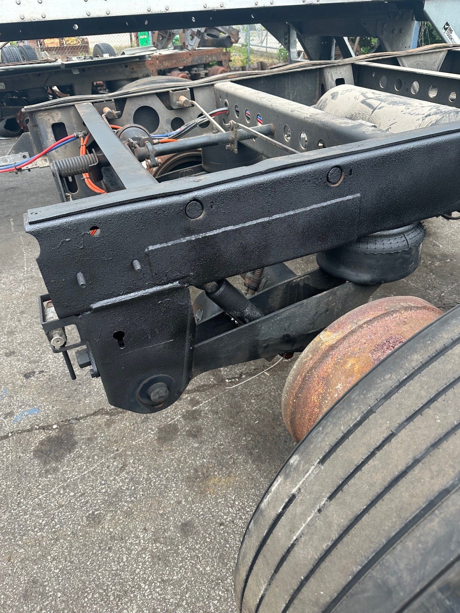 The black metal frame and suspension system of a semi-trailer, showing an air spring, shock absorber, and truck tire.