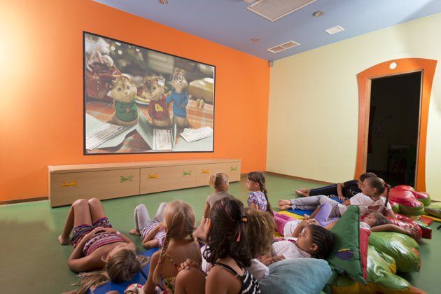 Un groupe d'enfants est allongé par terre et regarde un film sur un grand écran.