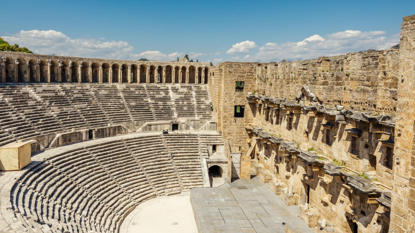 Ancient stone amphitheater with tiered seating and weathered ruins under a blue sky
