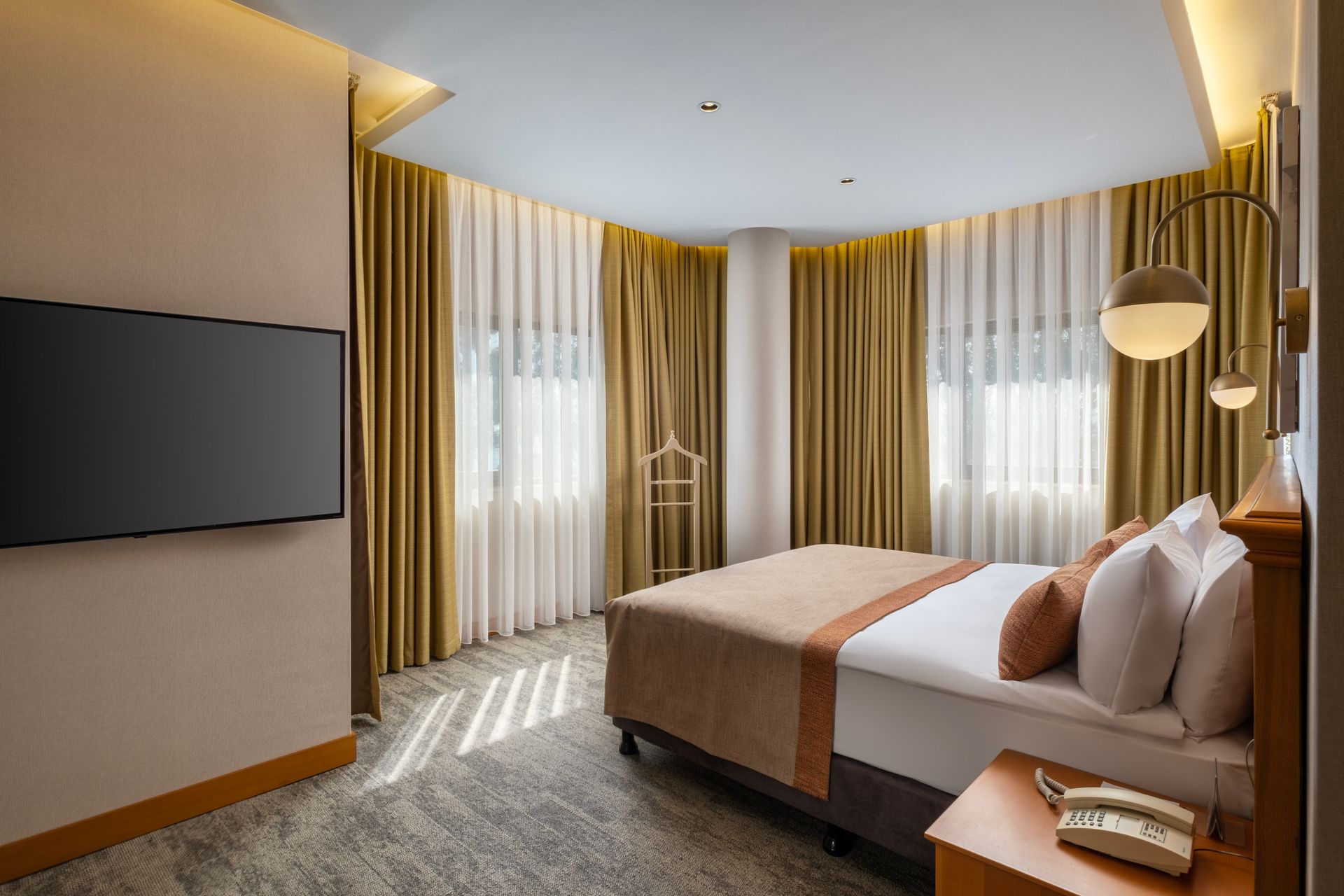 A hotel room with a bed , television , nightstand and curtains.