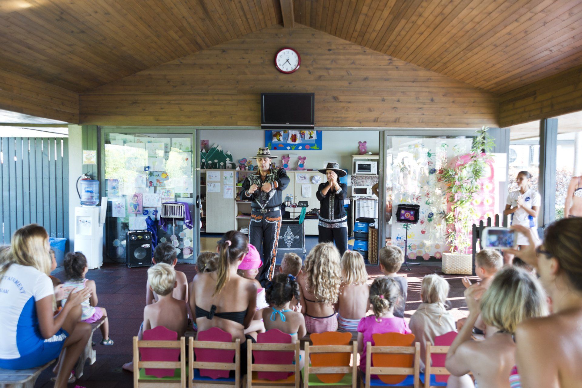 A group of children are sitting in a room watching a man play a violin.