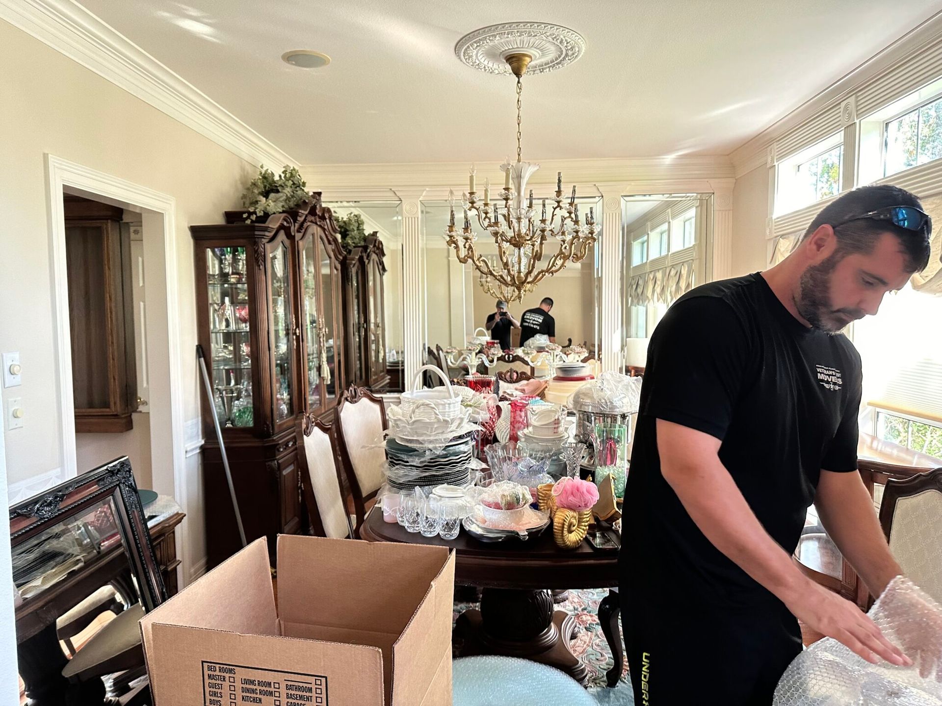 A Veteran's Best Movers crew member wrapping dishes in a dining room, with a moving box in front