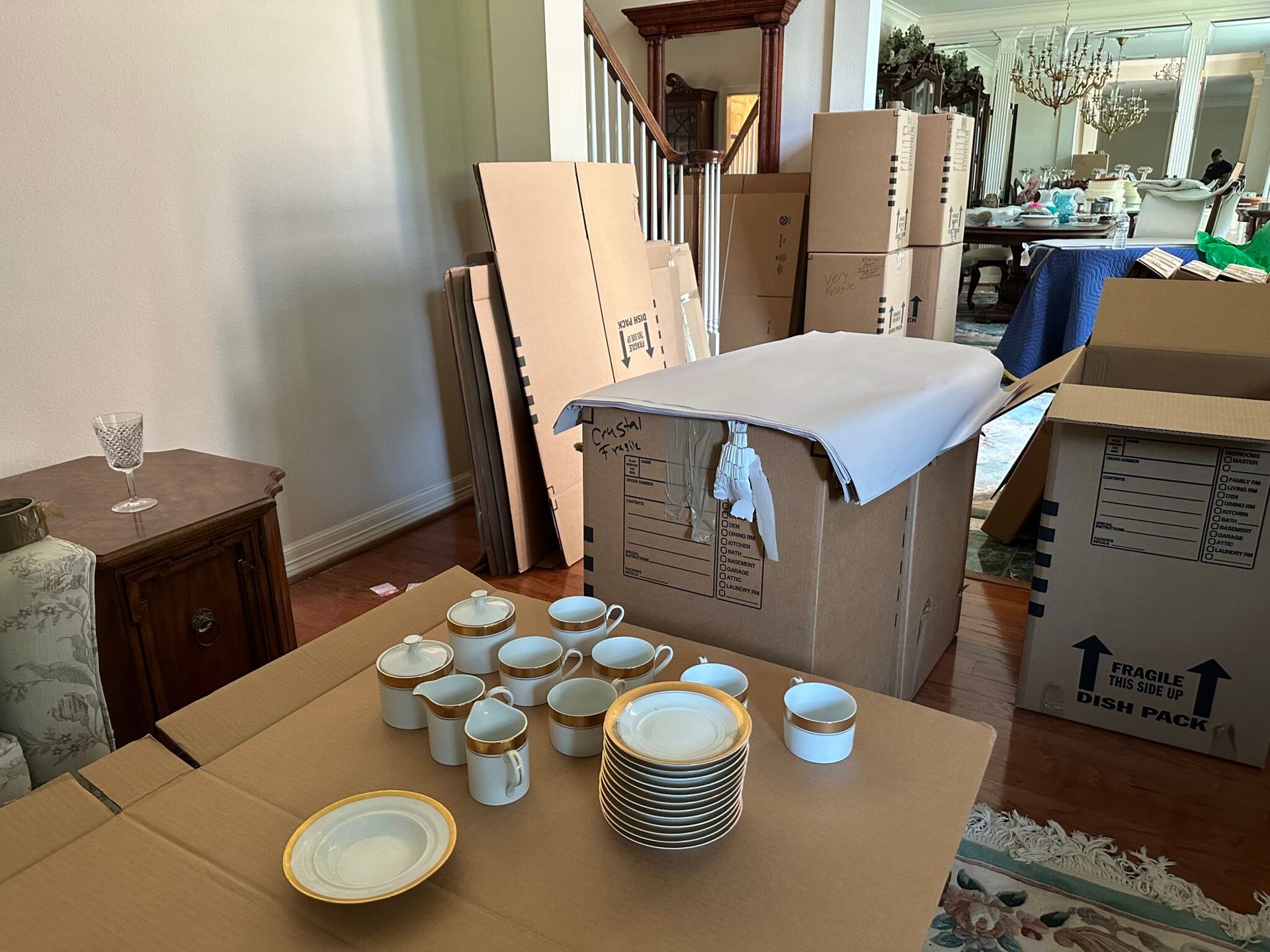 Gold rimmed china plates and cups laid out on packing paper beside moving boxes