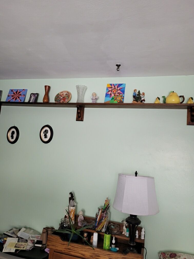 A long wooden shelf mounted on a pale green wall, decorated with various small objects, artwork, and a yellow teapot.