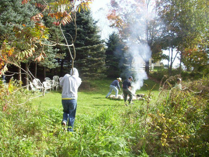 Hard work... good for the body, mind & soul. a group of people are picking up sticks and gathered around a fire in a backyard