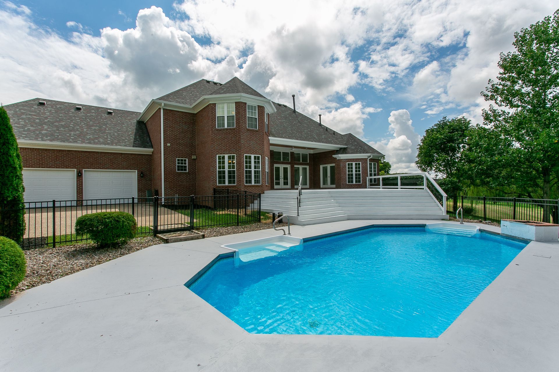 Backyard with a brick house and covered pool beside a bright blue swimming pool under a cloudy sky