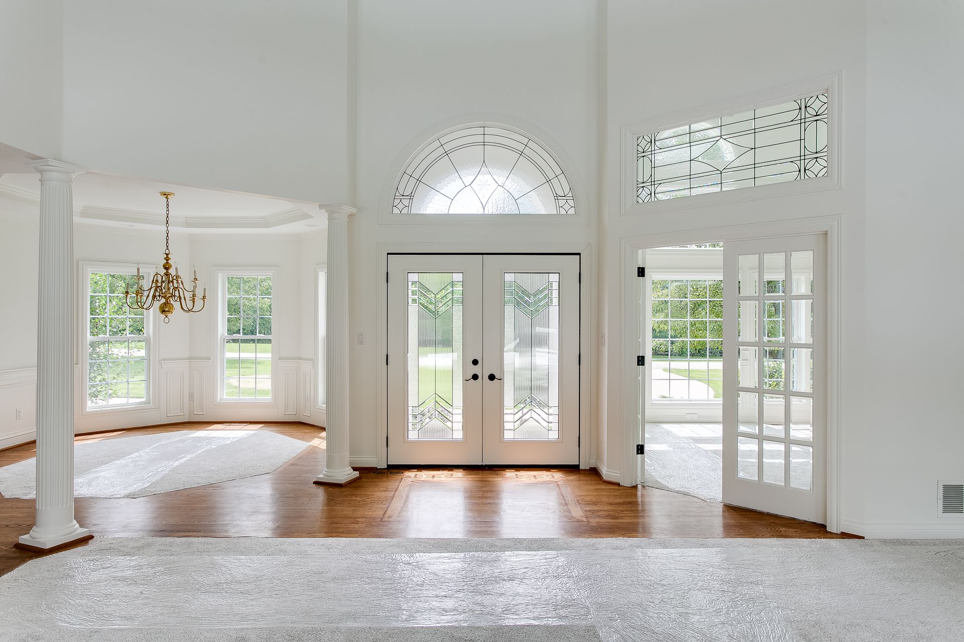 Bright, empty white living room with hardwood floors, arched windows, and glass double doors to a patio