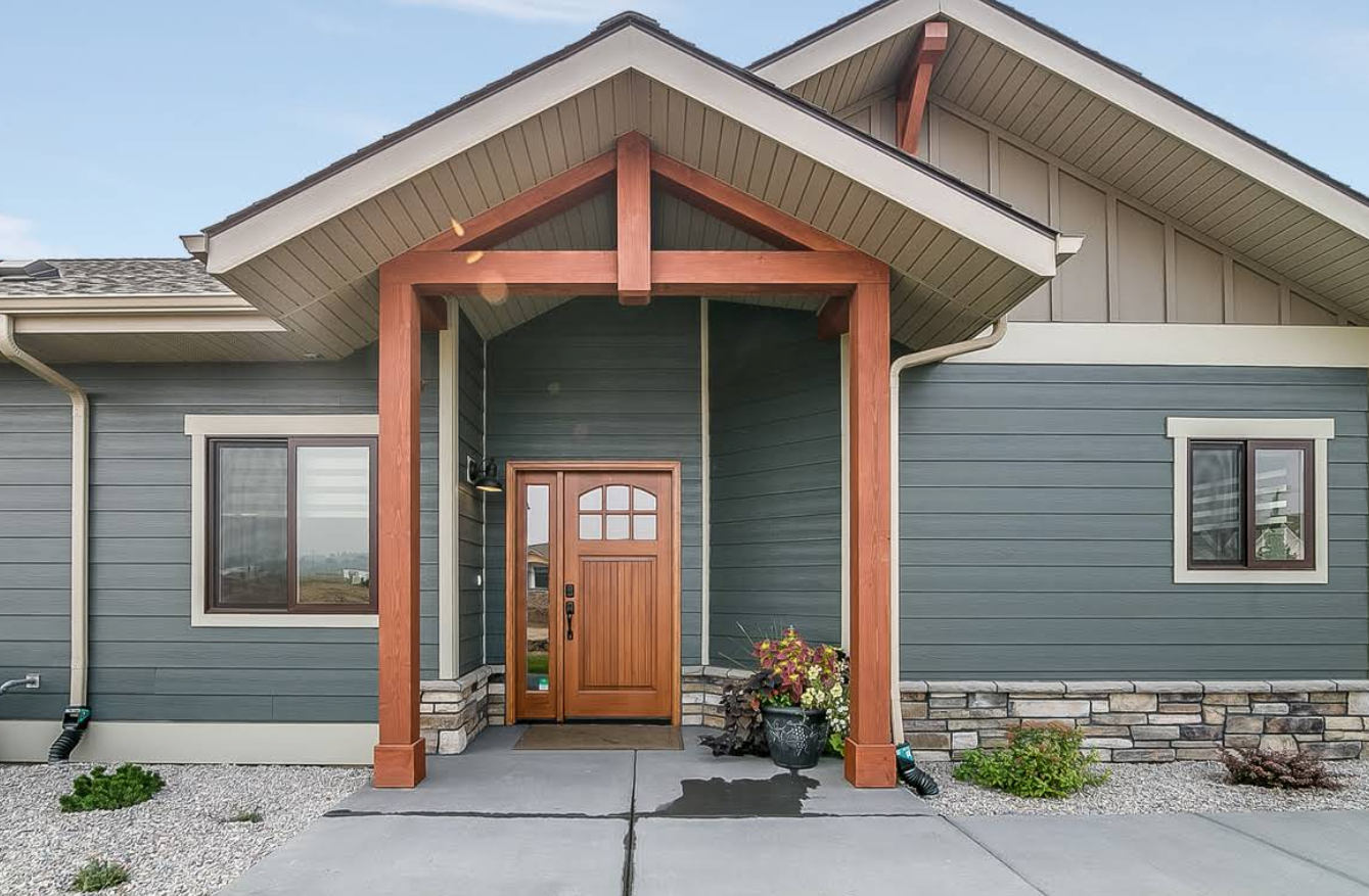 Front entrance of a house with a covered porch, wooden door, and blue-gray siding