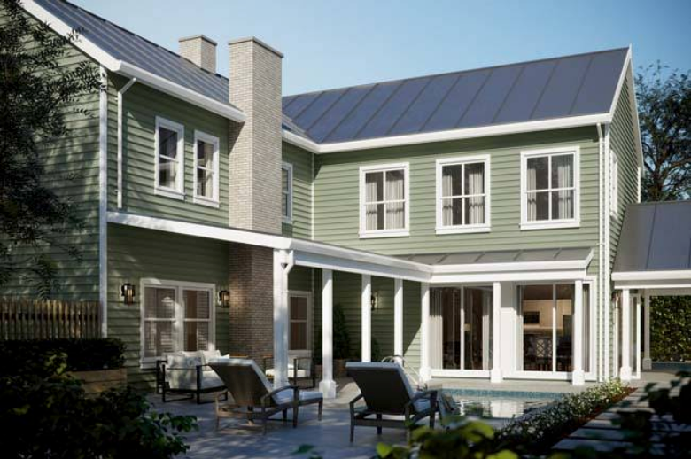 Two-story green house with a patio, outdoor chairs, and large windows in a sunny backyard