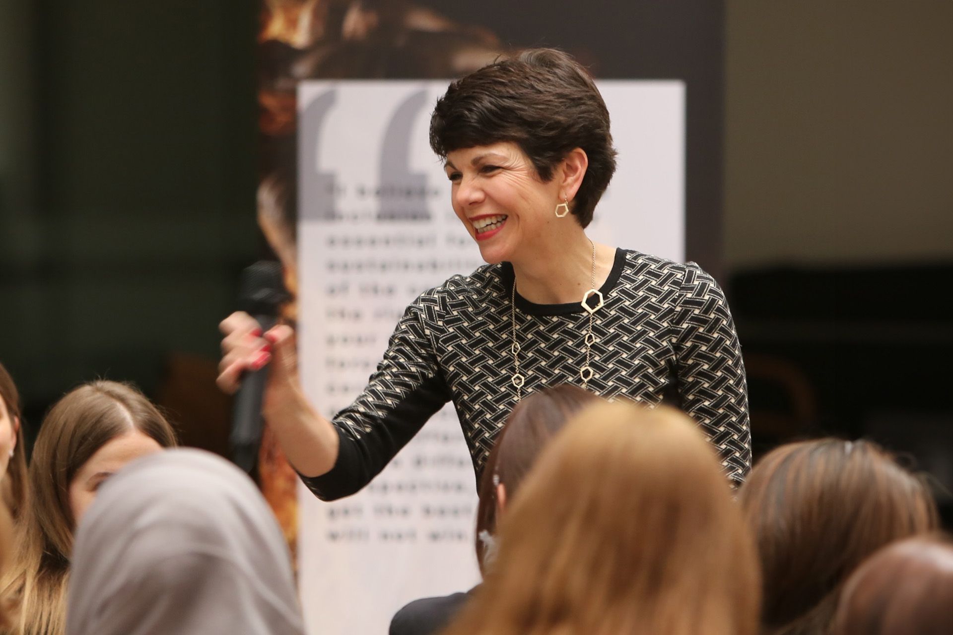 A woman stands in front of a crowd holding a microphone