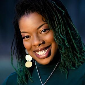 A woman with green dreadlocks and earrings is smiling for the camera.