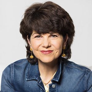 A woman wearing a denim jacket and earrings is smiling for the camera.