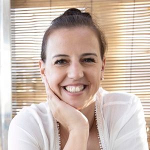 A woman in a white shirt is smiling with her hand on her chin.